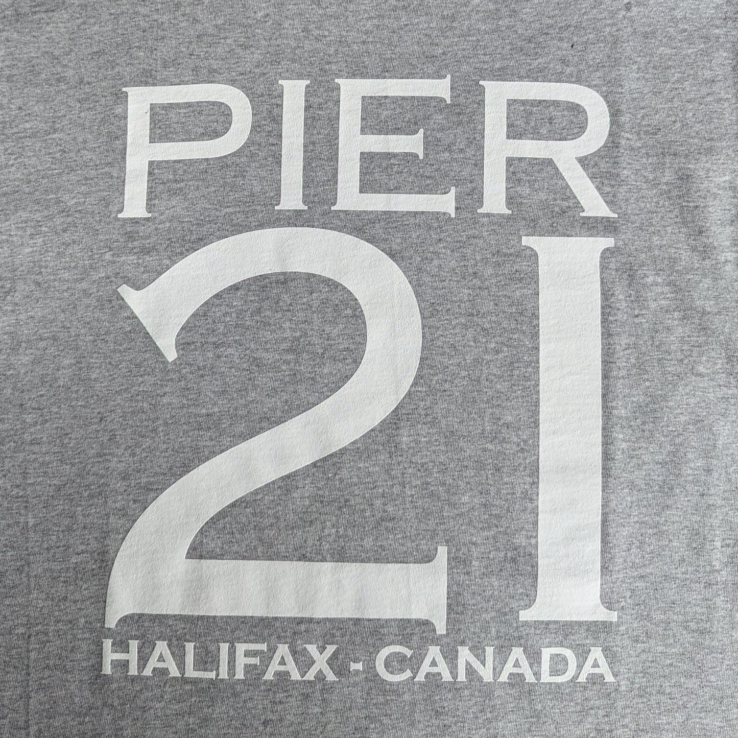 Close up of white lettering that say Pier 21 Halifax Canada on an athletic grey t-shirt