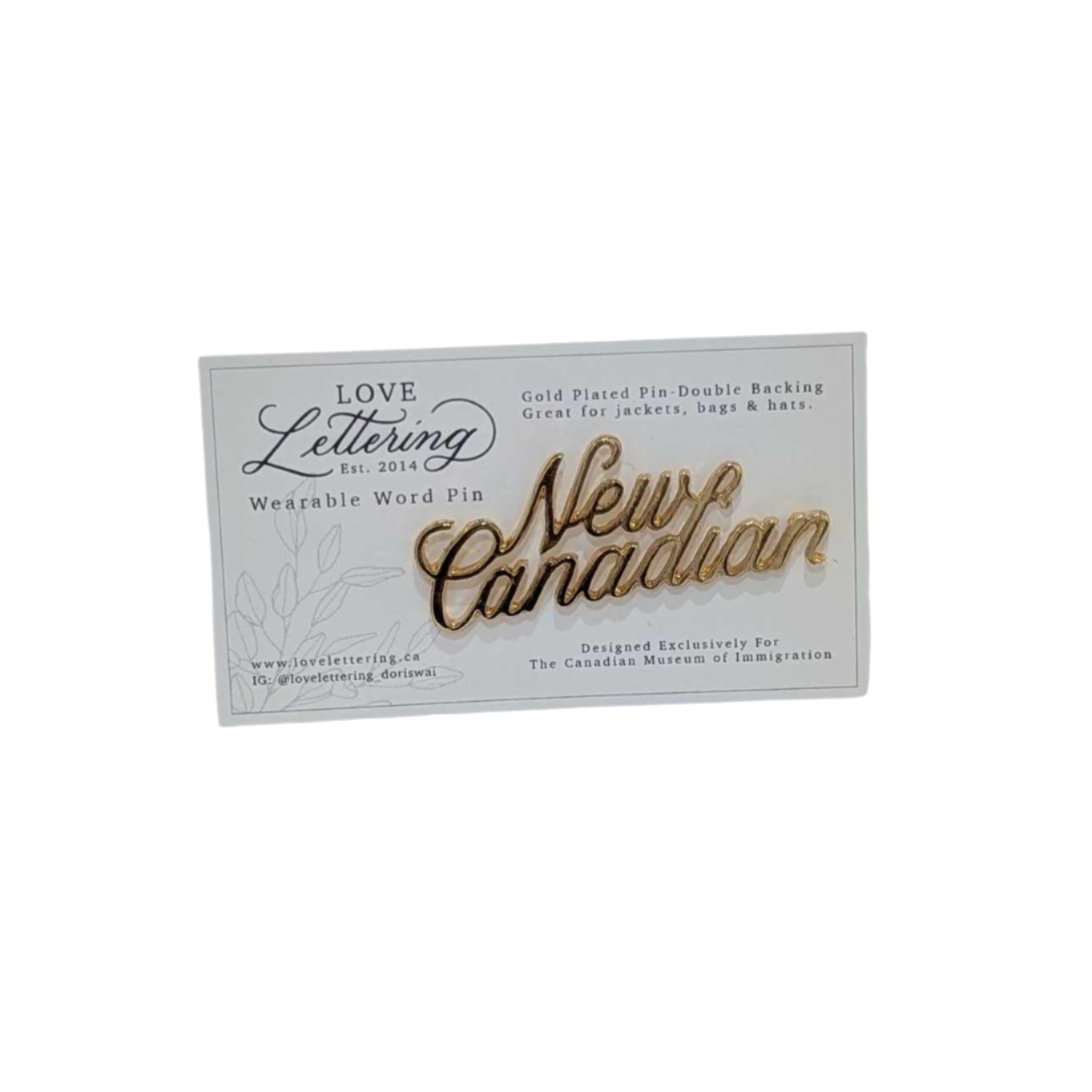 Gold pin saying New Canadian in cursive writing on a white backing card with logo of artisan