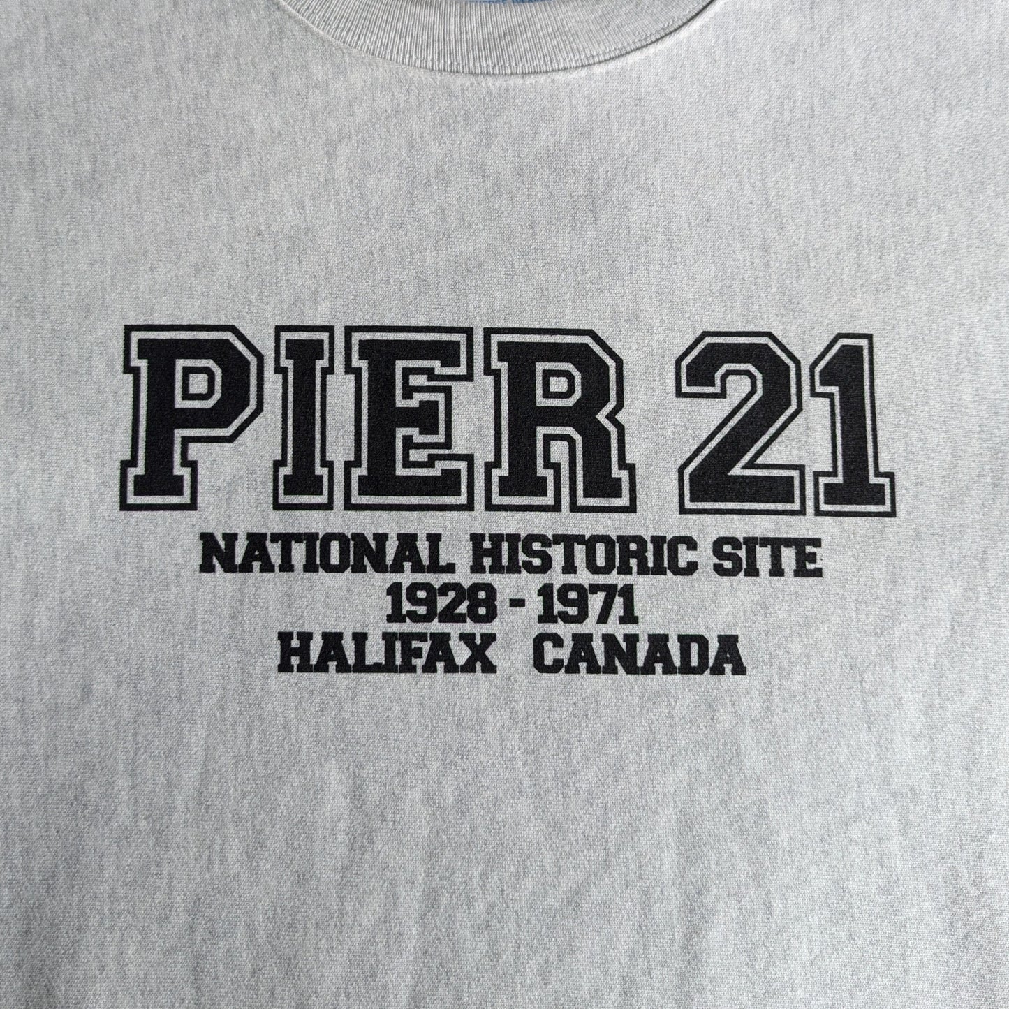 Pier 21 in varsity lettering with National Historic Site 1928-1971 Halifax Canada below. Black lettering on grey sweatshirt.
