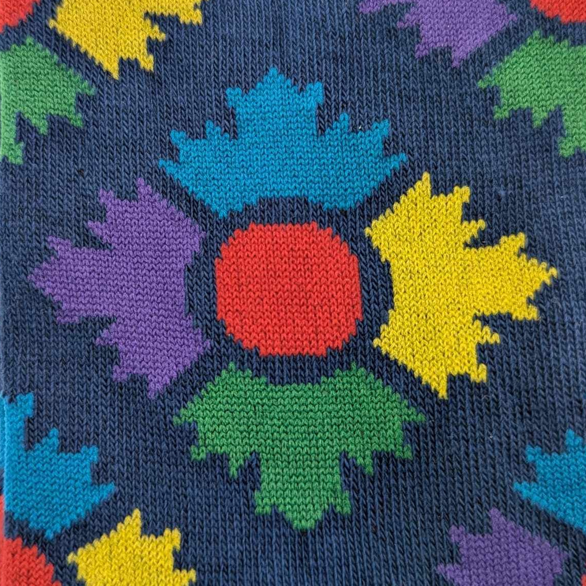 Close up of museum icon on a navy sock. The icon is four maple leaves in blue, yellow, green and purple with a red circle in the middle