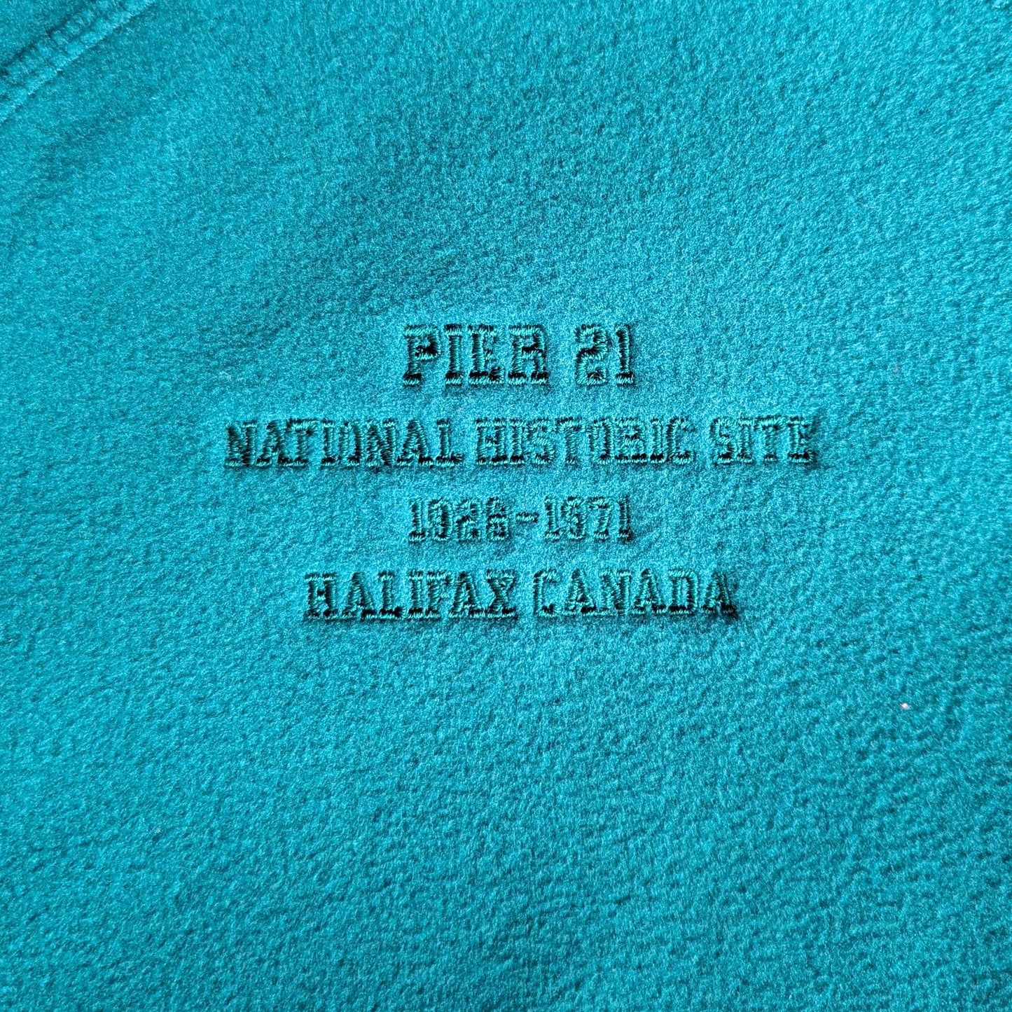 Close up of embroidery on the right breast on the green zip up that says Pier 21 National Historic Site 1928-1971 Halifax Canada 