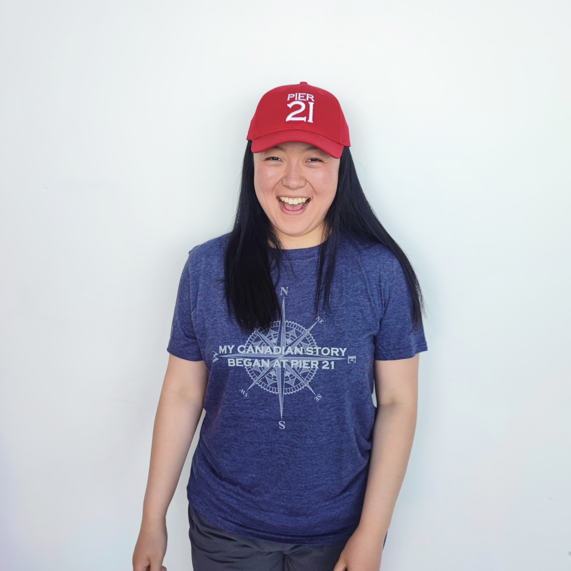 Female model wearing red Pier 21 hat and navy My Canadian Story Began at Pier 21 t-shirt 