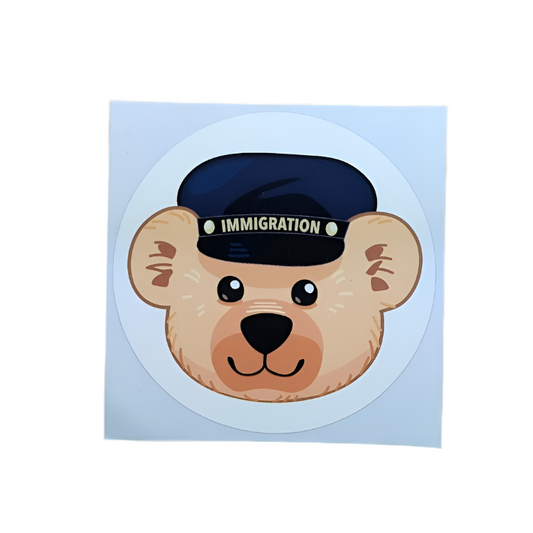 Round sticker on square background with a beige teddy bear face and a blue immigration cap on it's head