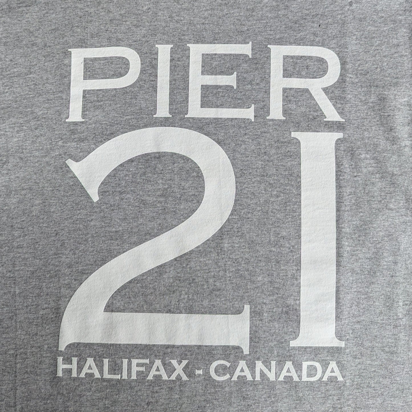 Close up of white lettering that say Pier 21 Halifax Canada on an athletic grey t-shirt 