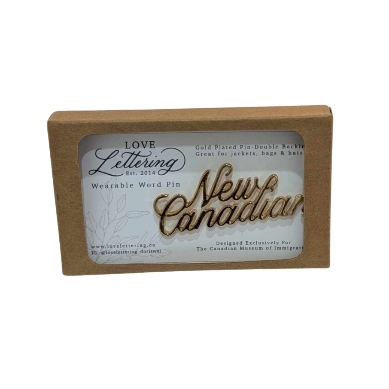 Gold pin with New Canadian in cursive writing inside of brown box