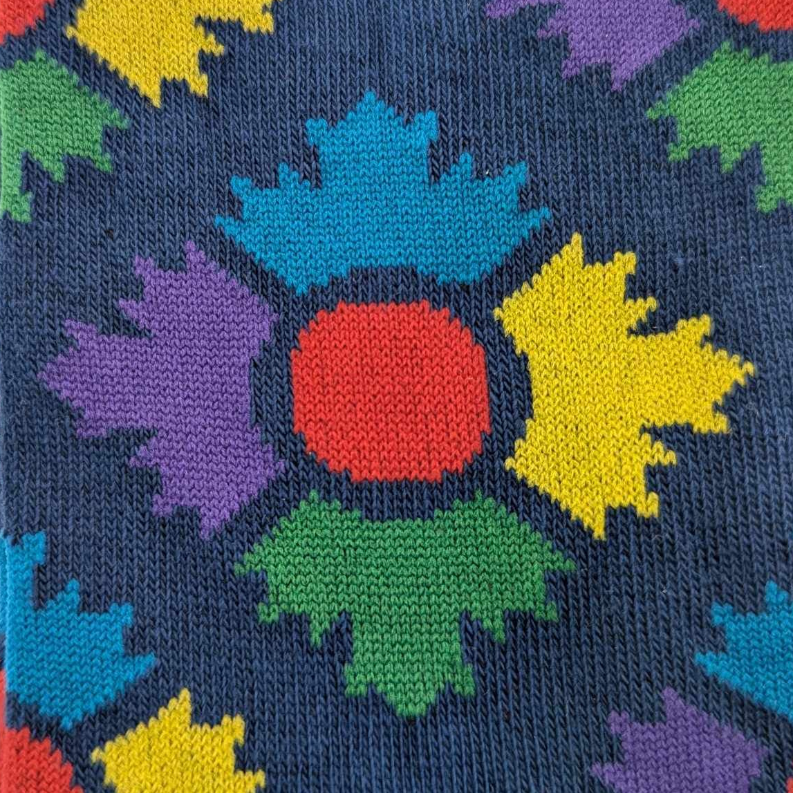 Close up of museum icon on a navy sock. The icon is four maple leaves in blue, yellow, green and purple with a red circle in the middle 